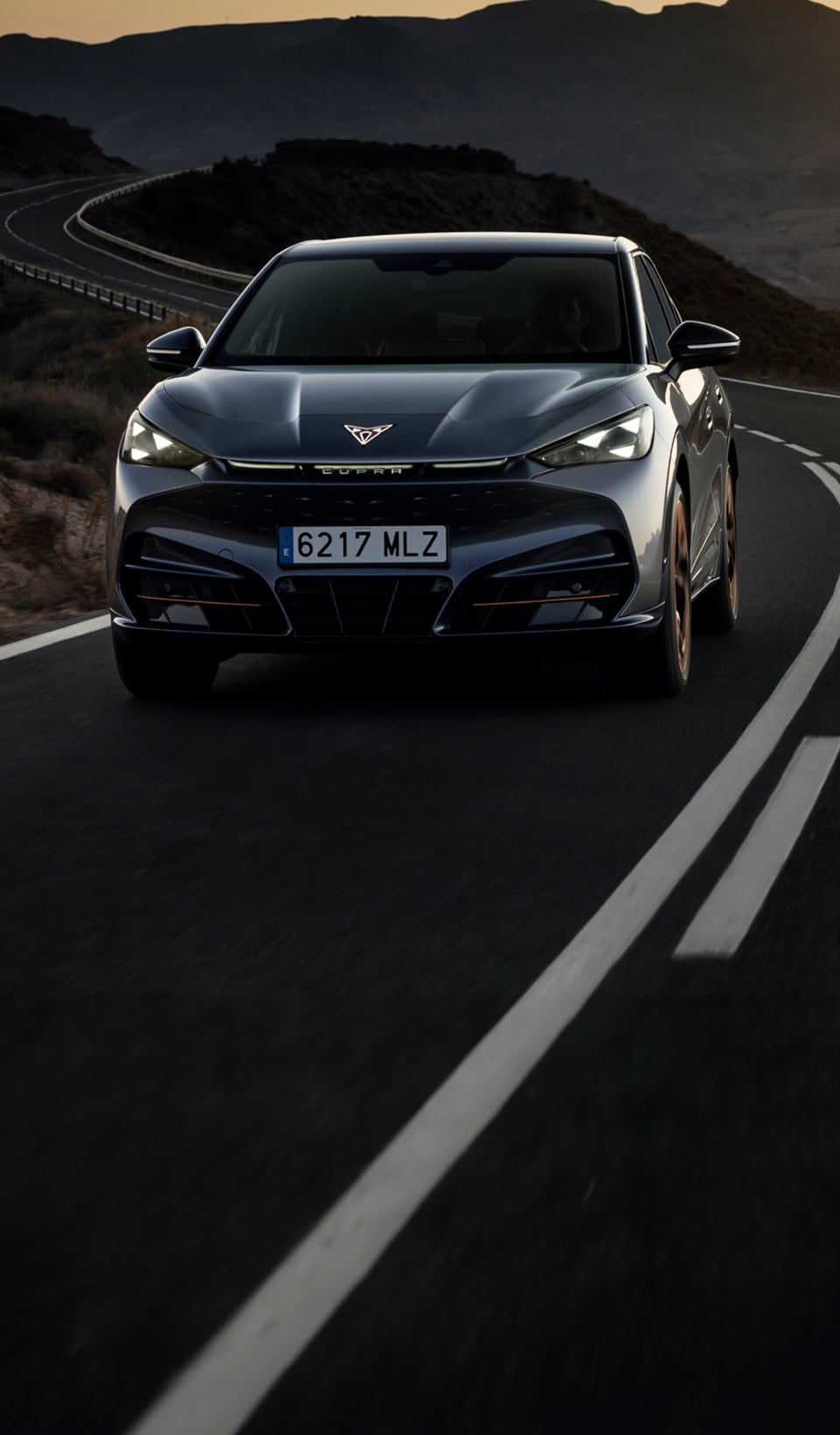 A dynamic scene featuring a CUPRA car in a sleek dark metallic color, positioned beside a blurred figure of a woman in a white dress using a VR headset and holding a conductor’s baton. 