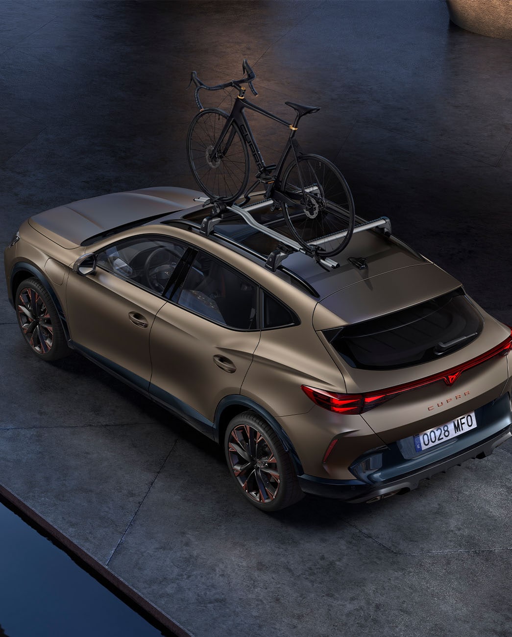 Yleiskuva uudesta Century bronze matt -värisestä CUPRA Formentorista, jossa polkupyöräteline, pysäköitynä betonille ilta-auringossa.