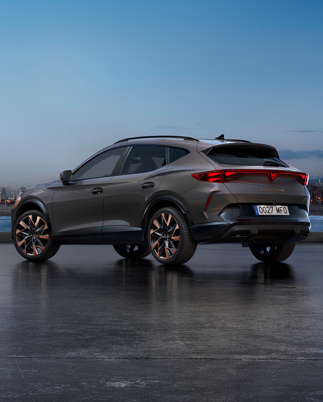 Uusi Graphene grey -värinen CUPRA Formentor pysäköitynä kävelykadulle veden ääreen iltahämärässä. Taustalla on kaupunkisiluetti sekä pilvenpiirtäjiä ja palmuja laskevan ilta-auringon valossa.