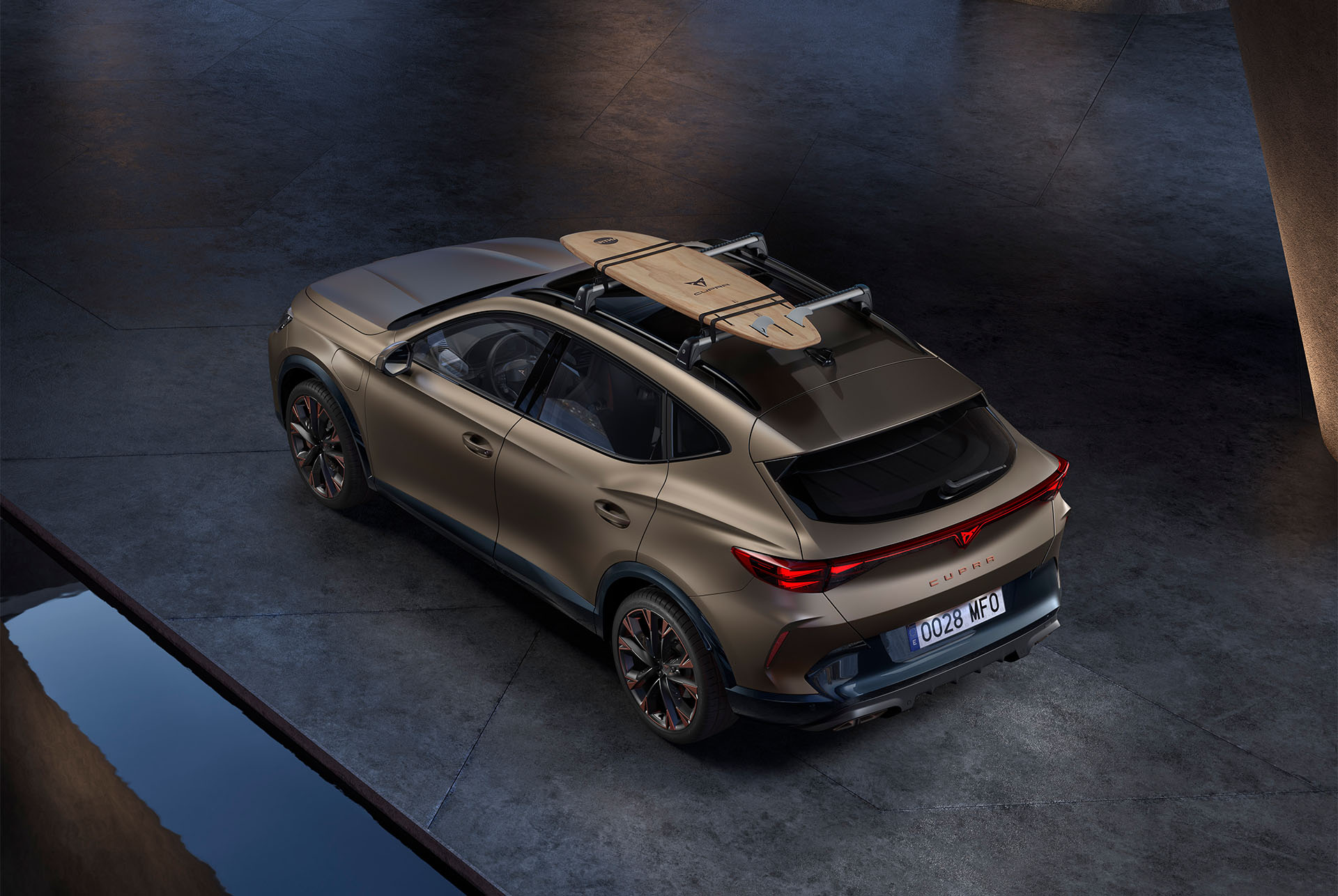 Yleiskuva uudesta Century bronze matt -värisestä CUPRA Formentorista, jossa surffilautateline katolla, auto pysäköitynä sementtialustalle.